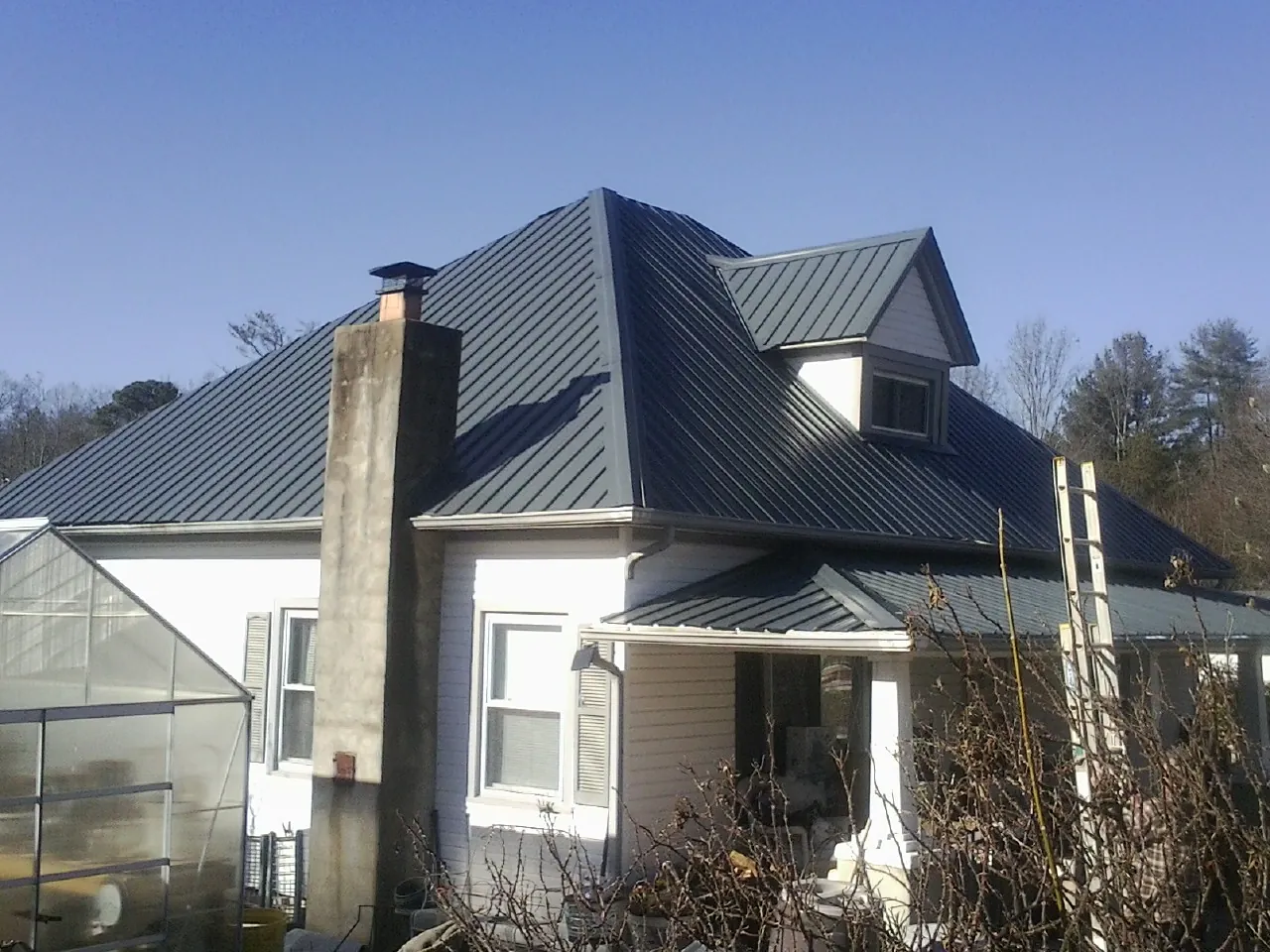 Dark blue standing seam metal roof on a white farmhouse with dormer — Slate & Tile Roof Repair by Roofing Brothers in Dunkirk